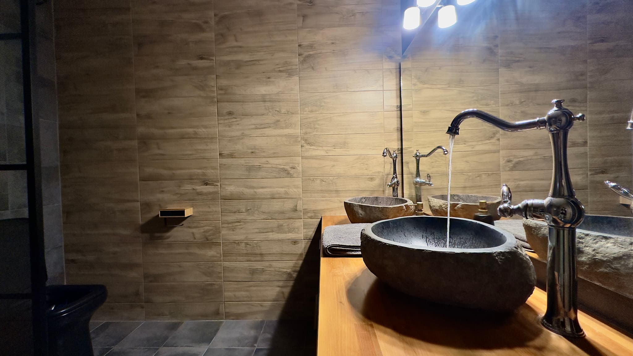 Double stone vessel sinks with warm wood vanity and ambient lighting